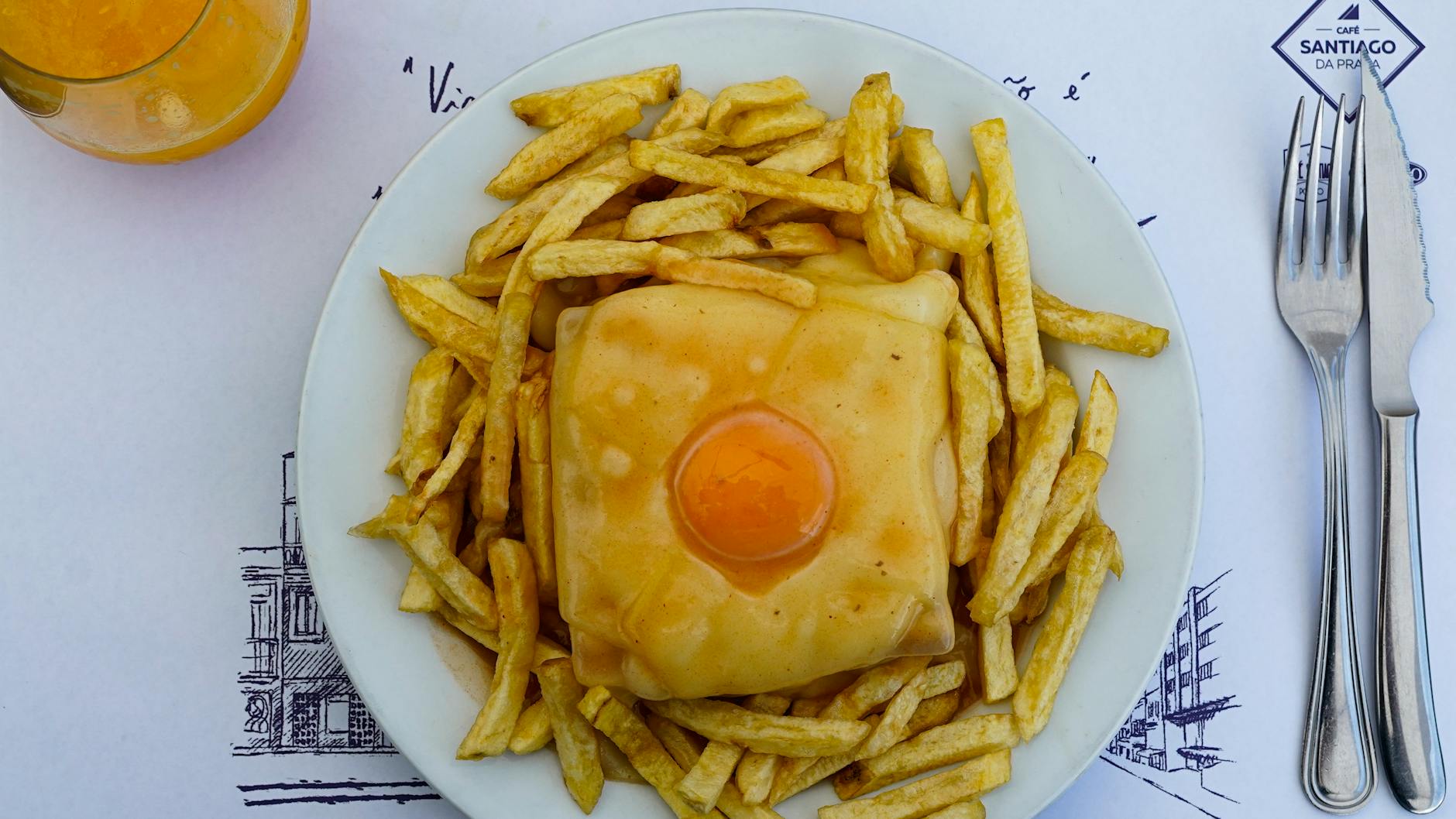 Portugalska kanapka francesinha z jajkiem, frytkami i szklanką soku