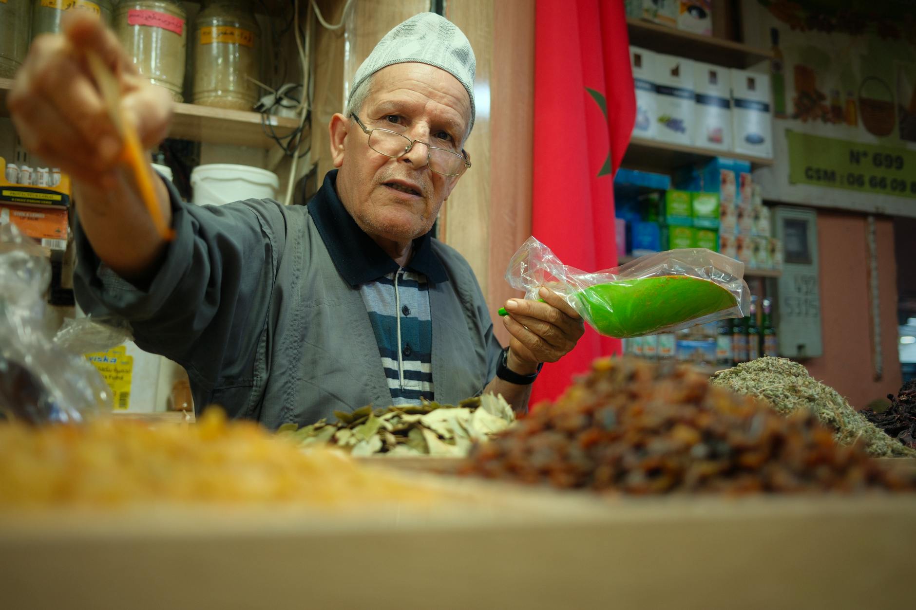 Starszy sprzedawca przypraw na marokańskim bazarze pokazuje kolorowe mieszanki