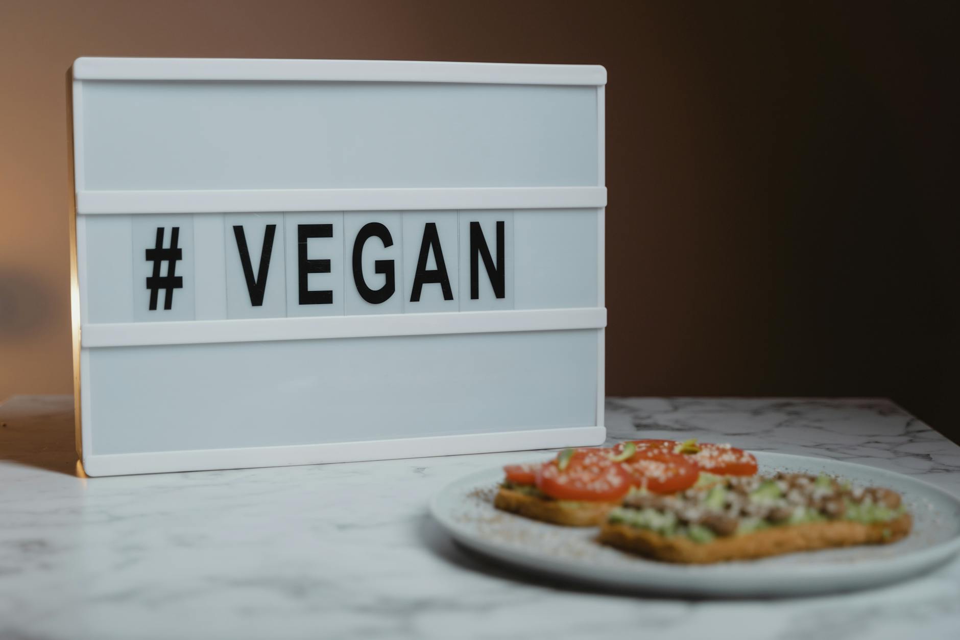 Tost z awokado na talerzu obok napisu hashtag VEGAN na marmurze