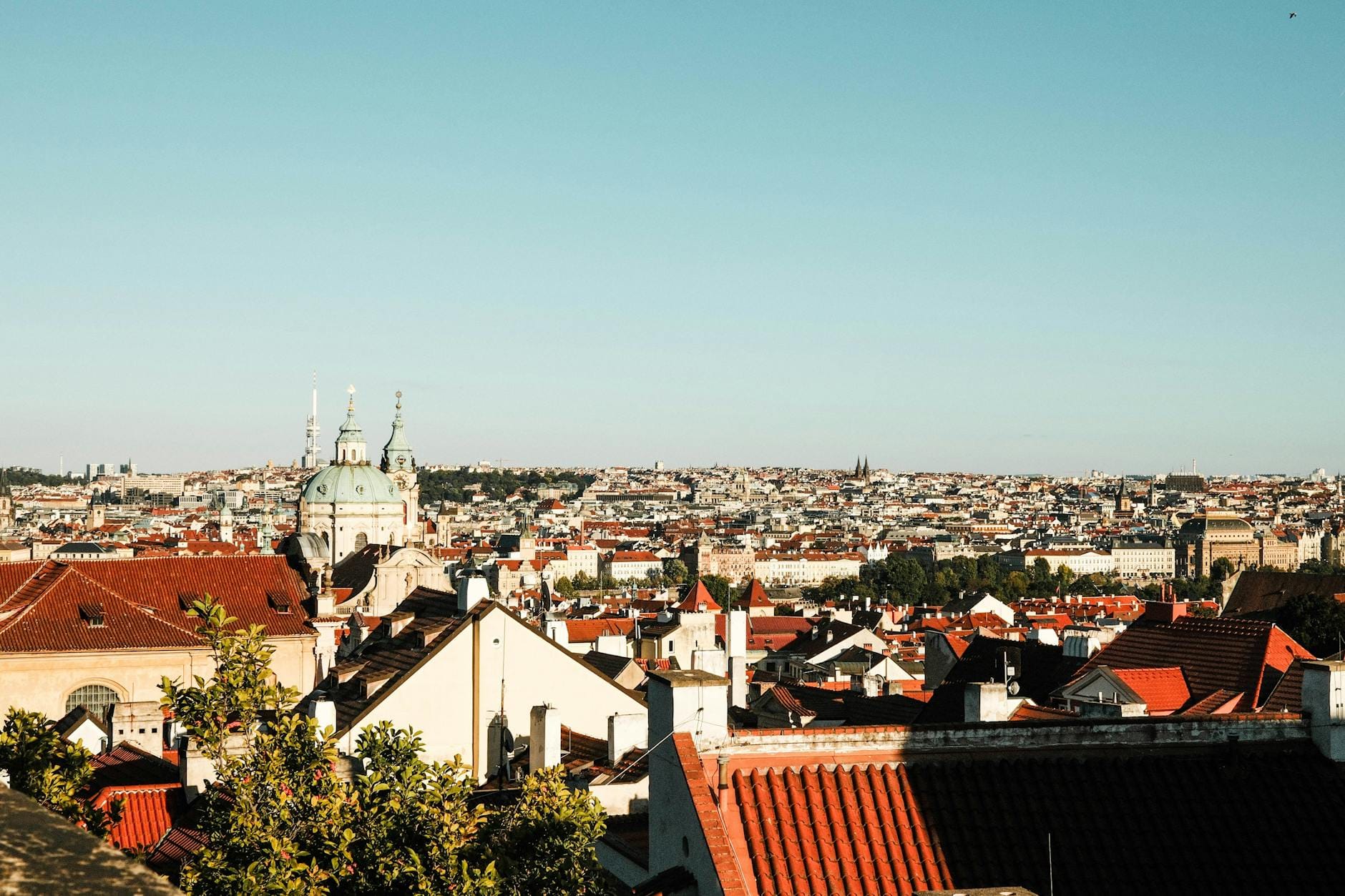 Panorama Pragi z czerwonymi dachami i zabytkową zabudową pod błękitnym niebem