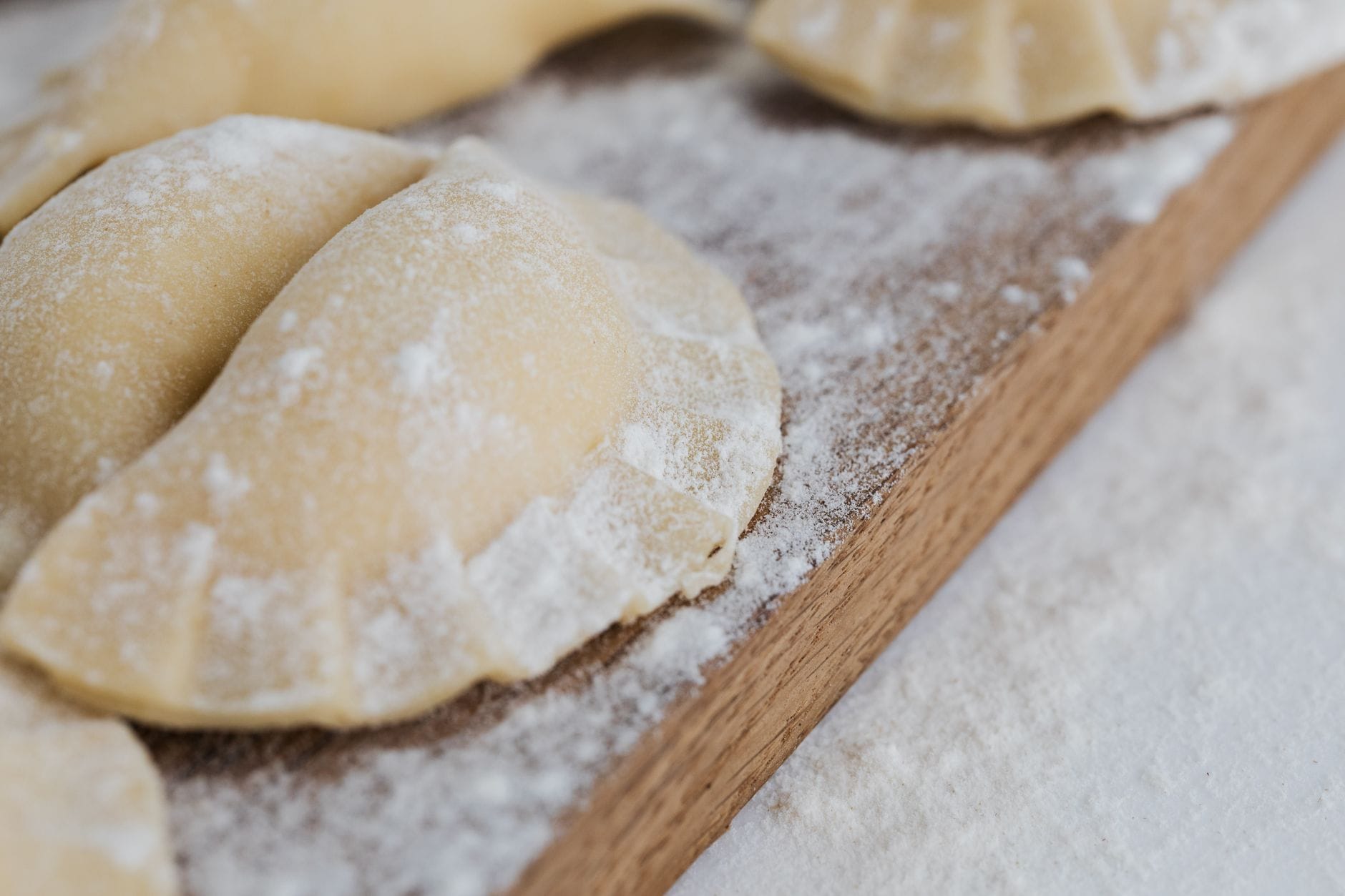 Świeżo lepione pierogi oprószone mąką na drewnianej desce